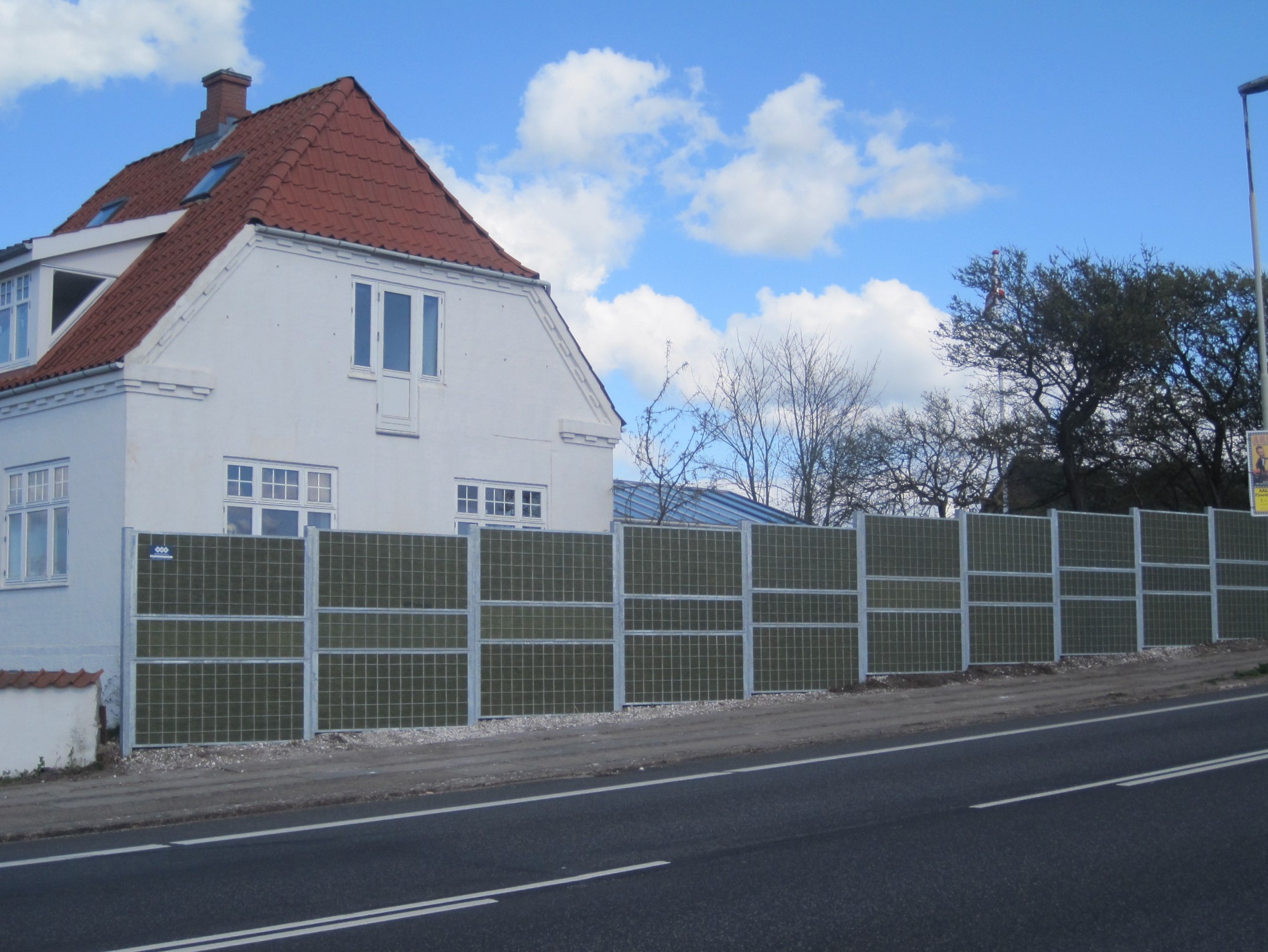 Ein Noistop® Steel-Lärmschutzzaun von Poda Zaun wurde vor einem Haus an einer Hauptstraße aufgestellt, um den Verkehrslärm abzuschirmen